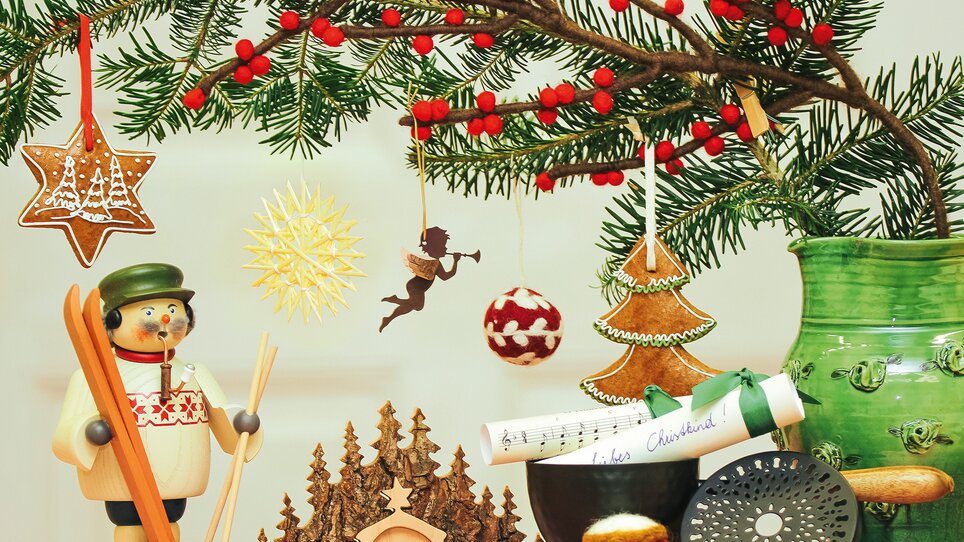 A festively decorated table with Christmas ornaments, a wooden figure, and green branches | © VK Stmk