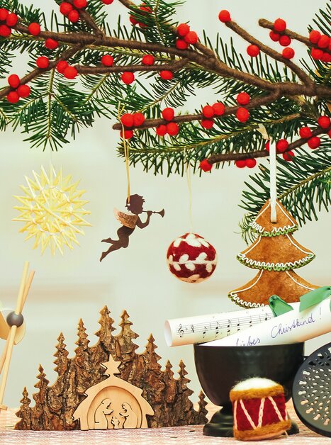A festively decorated table with Christmas ornaments, a wooden figure, and green branches | © VK Stmk