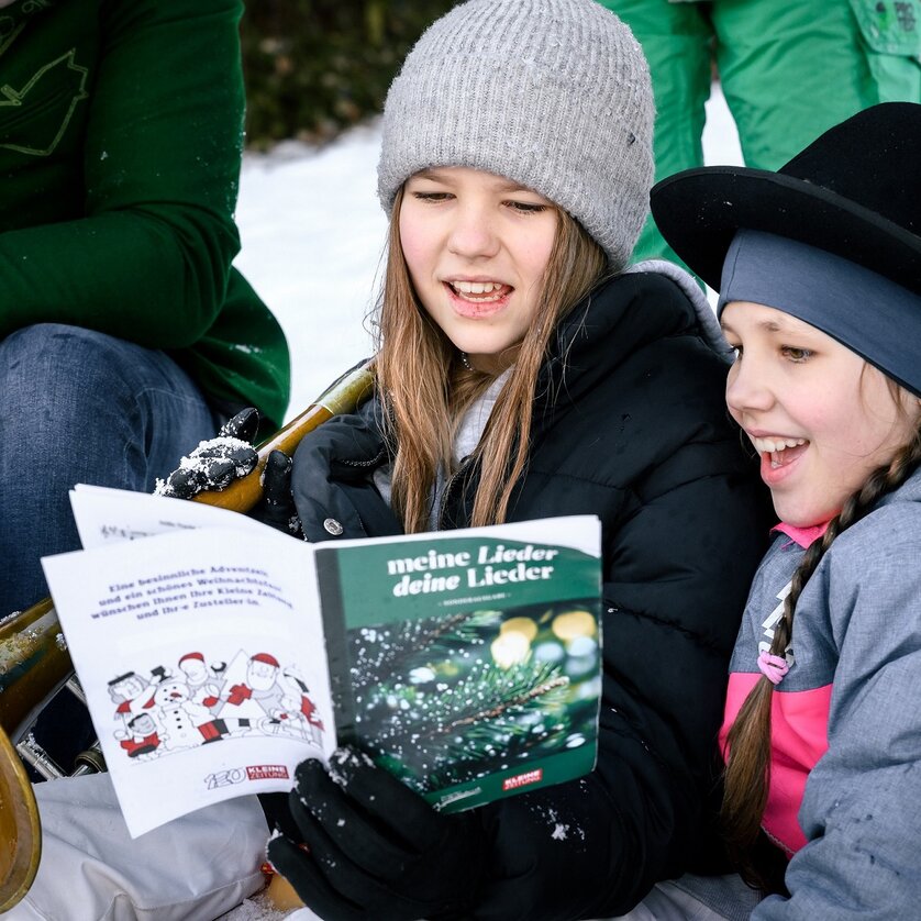 Zwei Mädchen freuen sich beim Singen von Weihnachtsliedern im Schnee. | © Ulrike Rauch