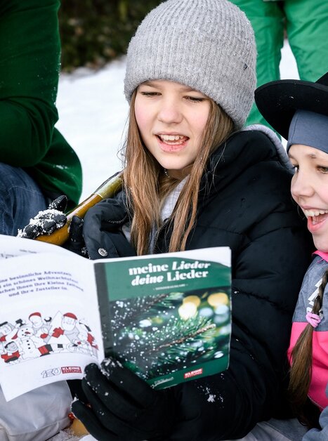 Two girls enjoy singing Christmas songs in the snow. | © Ulrike Rauch
