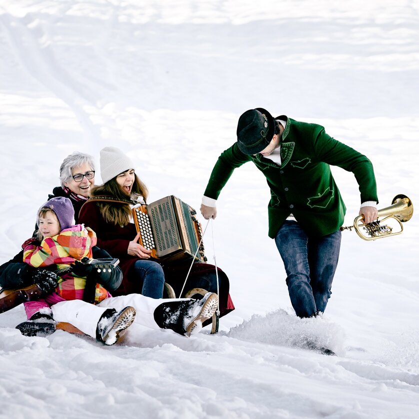 Eine Familie im Schnee sitzt auf einem Schlitten und spielt Musik. | © Ulrike Rauch