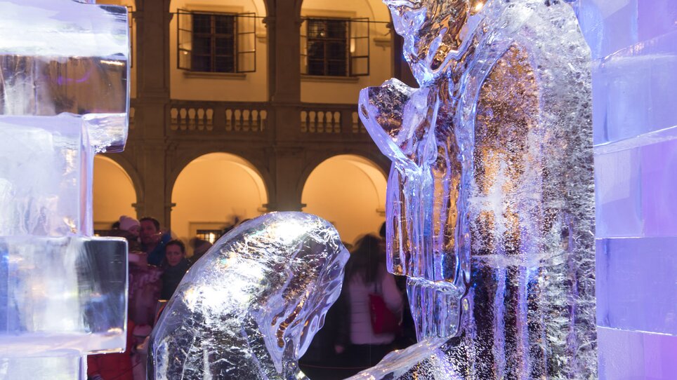 Eine Eiskrippe dargestellt in einem beleuchteten Innenhof mit Menschen im Hintergrund. | © Graz Tourismus - Foto Fischer