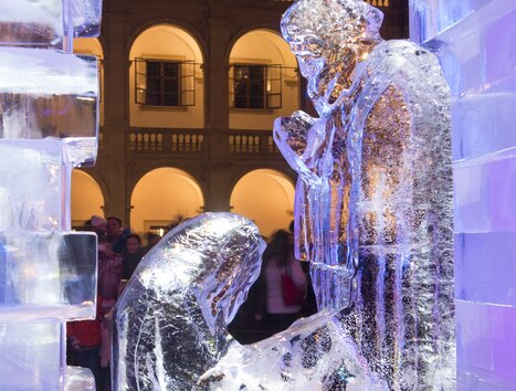 Eine Eiskrippe dargestellt in einem beleuchteten Innenhof mit Menschen im Hintergrund. | © Graz Tourismus - Foto Fischer