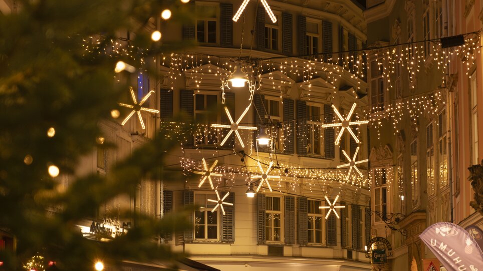 Strada illuminata a Graz con luci di Natale e stelle, persone a passeggio. | © Vincent Croce