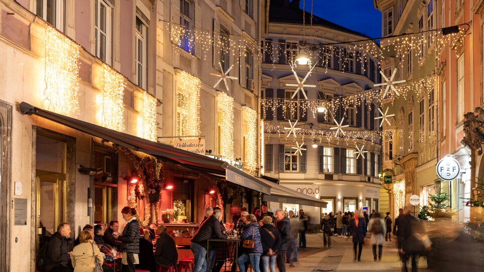 Affollata Stempfergasse a Graz, decorata con luci e persone che godono di bevande. | © Graz Tourismus-Harry Schiffer