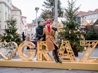 Paar posiert vor beleuchteter Graz-Dekoration im Weihnachtsmarkt. | © Graz Tourismus - Mias Photoart
