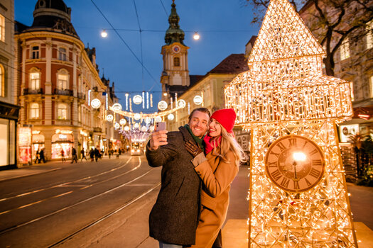 Pärchen macht ein Selfie vor beleuchtetem Uhrenturm in Graz. | © Graz Tourismus - Mias Photoart