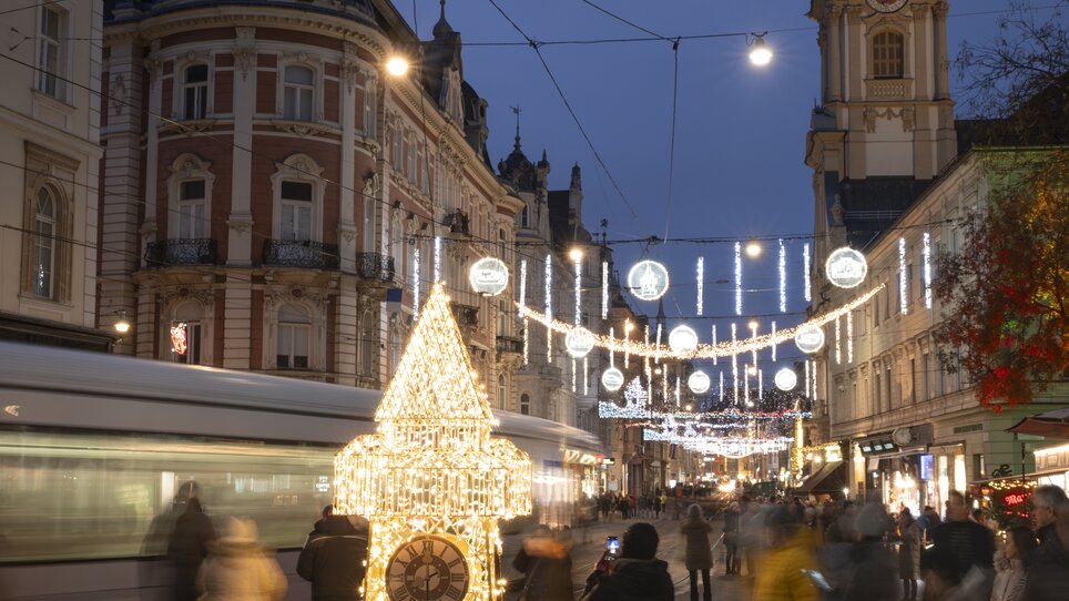Beleuchteter Uhrturm und geschäftige Straße in Graz zur Adventszeit. | © Vincent Croce