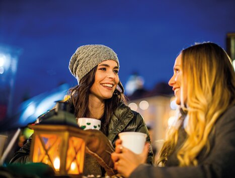 Two women laughing and enjoying hot drinks in the dark. | © Graz Tourismus - Tom Lamm