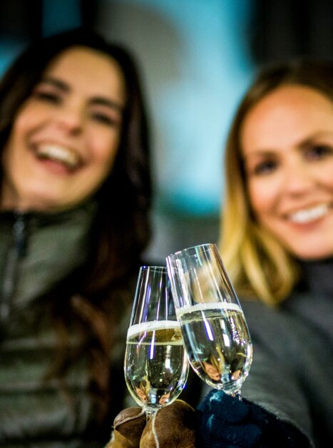 Zwei Frauen halten Sektgläser in der Nacht und lächeln. | © Graz Tourismus - Tom Lamm