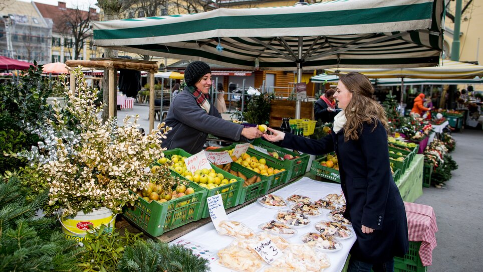 Auf dem Markt in Graz tauscht eine Frau frisches Obst mit einer Verkäuferin aus. | © Graz Tourismus - Tom Lamm