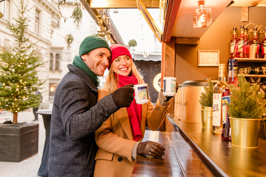 A couple enjoys warm drinks and smiles at a Christmas market in Graz. | © Graz Tourismus - Mias Photoart