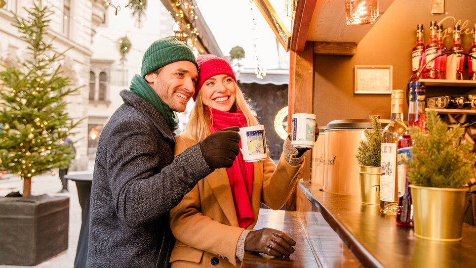 A couple enjoys warm drinks and smiles at a Christmas market in Graz. | © Graz Tourismus - Mias Photoart