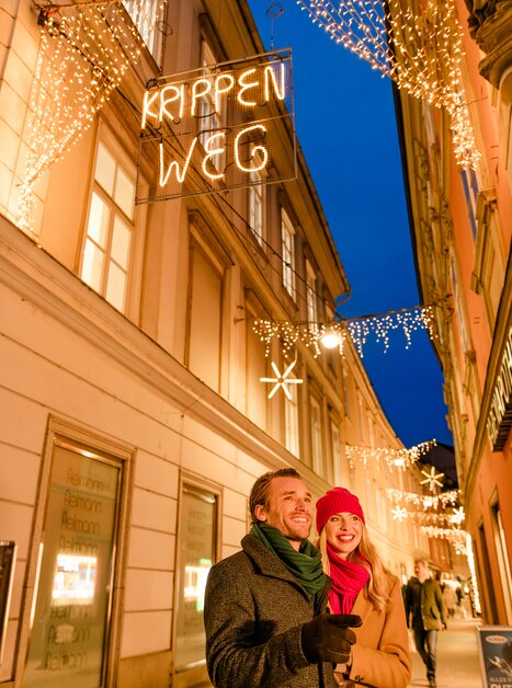 Couple in a Christmas-lit street in Graz, surrounded by festive lights and decorations. | © Graz Tourismus - Mias Photoart