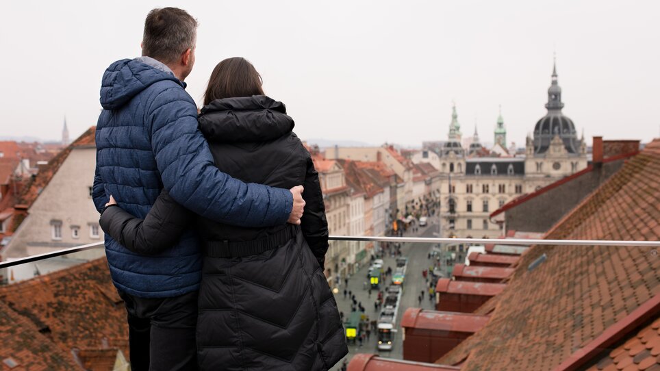 Couple looking from a terrace at the roofscape of Graz and the town hall. | © Graz Tourismus - Katja Stadler