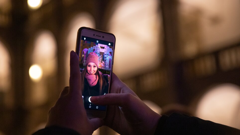 A woman takes a selfie in front of the festively illuminated ice cot in the Landhaus courtyard. | © Graz Tourismus - Katja Stadler