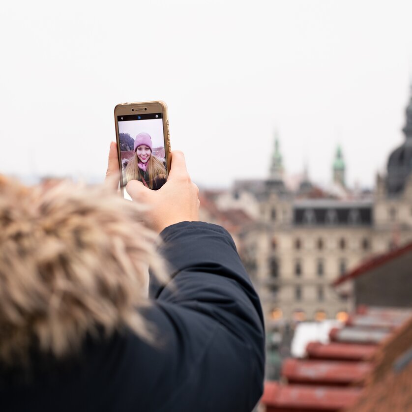 Una persona fa un selfie con Graz sullo sfondo in una giornata nuvolosa. | © Graz Tourismus - Katja Stadler