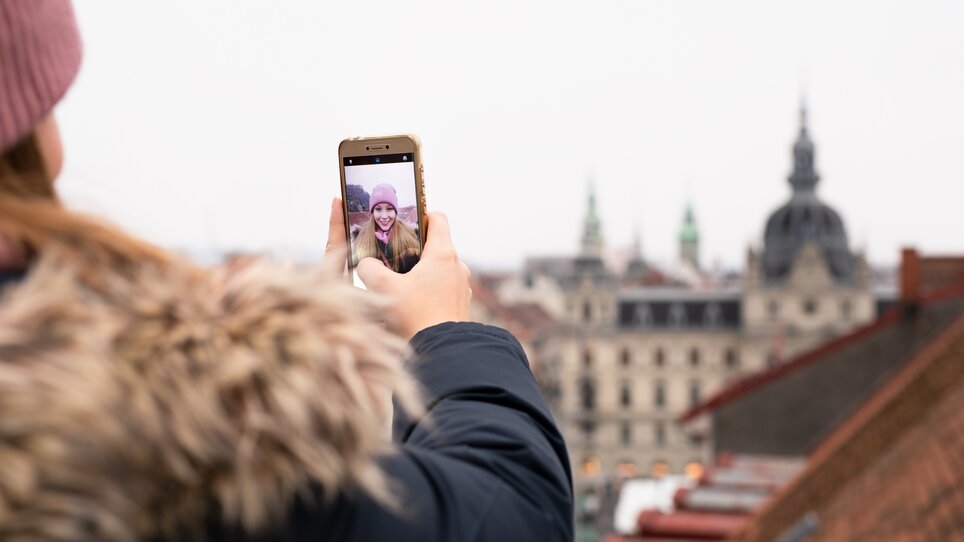 A person takes a selfie with Graz in the background on a cloudy day. | © Graz Tourismus - Katja Stadler