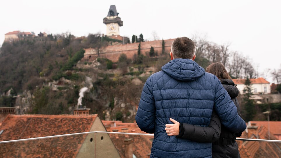 Couple embraces, view of the Graz Clock Tower and the city. | © Graz Tourismus - Katja Stadler