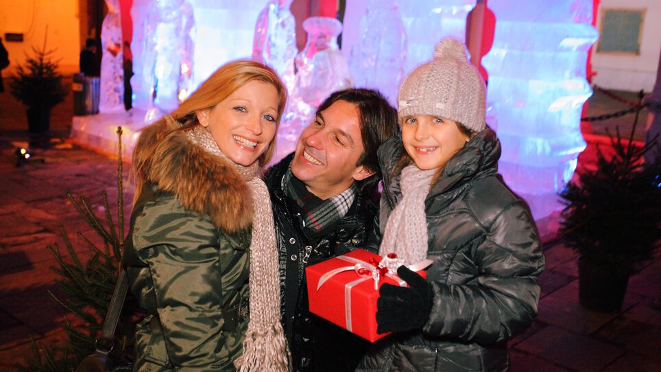 Familie posiert fröhlich vor beeindruckenden Eisskulpturen, Weihnachtsgeschenke in der Hand. | © Graz Tourismus - Max Wegscheidler