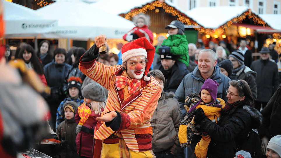 Ein Clown unterhält eine Menschenmenge auf einem Weihnachtsmarkt. | © Foto Jakotopia