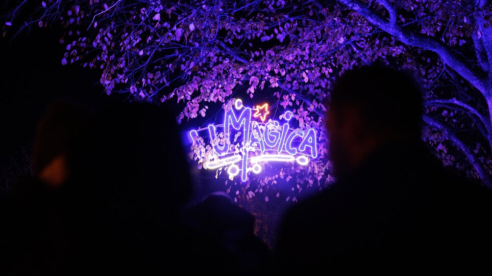 Bunte Lichter und Menschen vor einem leuchtenden Schild mit 'LUMAGICA'. | © Erwin Scheriau