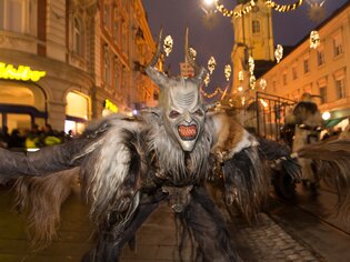 Ein Krampus mit gruseligem Gesicht und zotteliger Kleidung tanzt auf der Straße in Graz. | © Graz Tourismus - Harry Schiffer