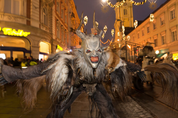 A Krampus with a frightening face and shaggy clothing dances on the street in Graz. | © Graz Tourismus - Harry Schiffer