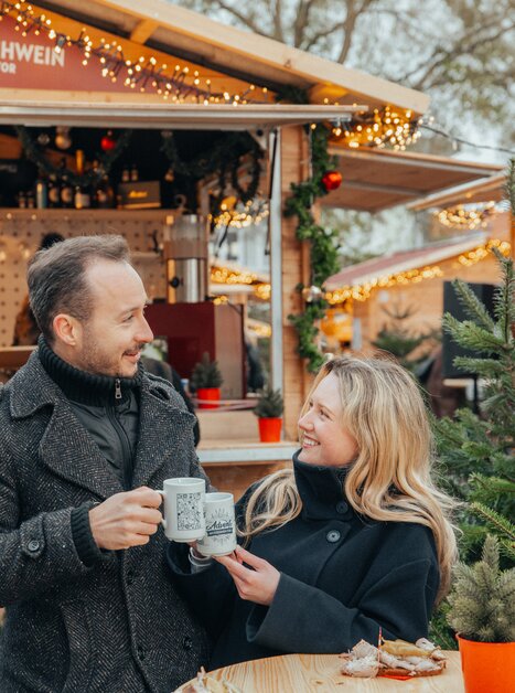 Couple in winter clothing enjoying mulled wine at the advent market. | © Mias Photoart
