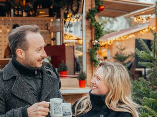 Paar in winterlicher Kleidung mit Glühwein am Adventmarkt. | © Mias Photoart