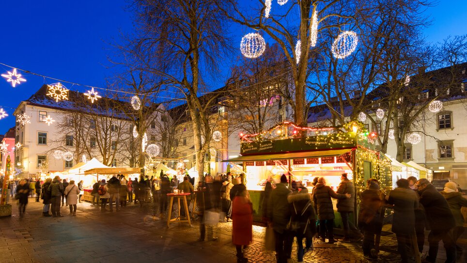 Advent in Graz I Handicraft market on Färberplatz square | © Graz Tourismus - Harry Schiffer Bustling Christmas market with lights, stalls, and people in Graz. | © Graz Tourismus - Harry Schiffer