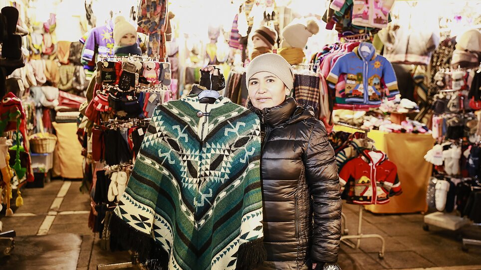 Eine Frau präsentiert einen bunten Poncho auf einem Markt. | © Thomas Luef
