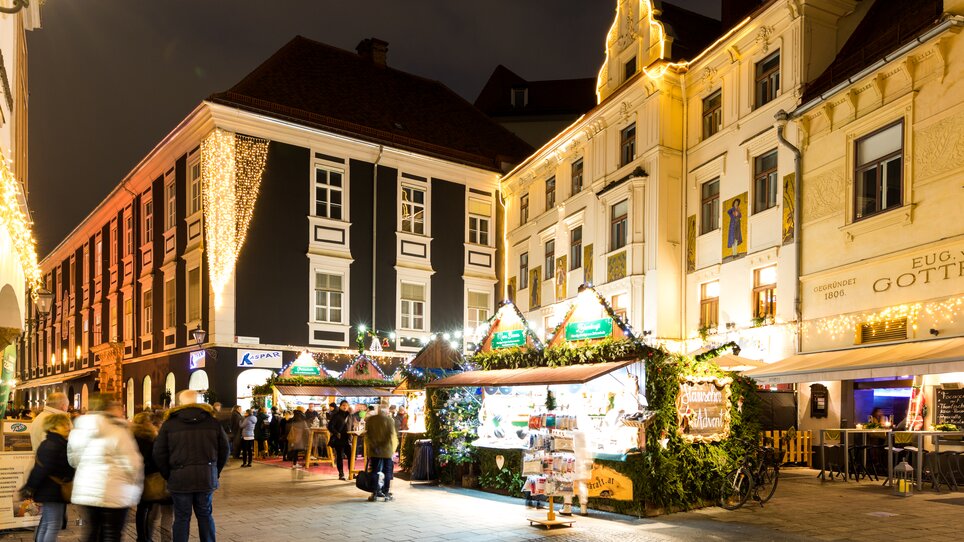 Blick auf den festlich beleuchteten Adventmarkt am Glockenspielplatz in Graz bei Nacht. | © Graz Tourismus - Harry Schiffer