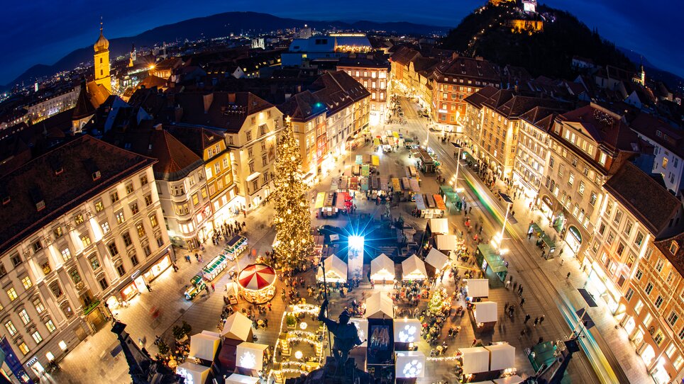Beleuchteter Christkindlmarkt mit Ständen am Hauptplatz von Graz, Grazer Uhrturm im Hintergrund. | © Graz Tourismus - Harry Schiffer