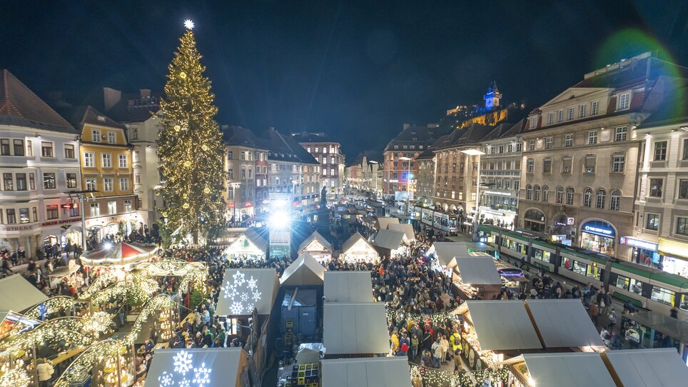 Nachtansicht des Christkindlmarkts in Graz mit beleuchteten Ständen und großen Weihnachtsbaum auf dem Hauptplatz. | © Stadt Graz Foto Fischer