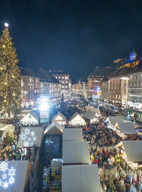 Vista notturna del mercatino di Natale a Graz con bancarelle illuminate e grande albero di Natale in Hauptplatz. | © Stadt Graz Foto Fischer