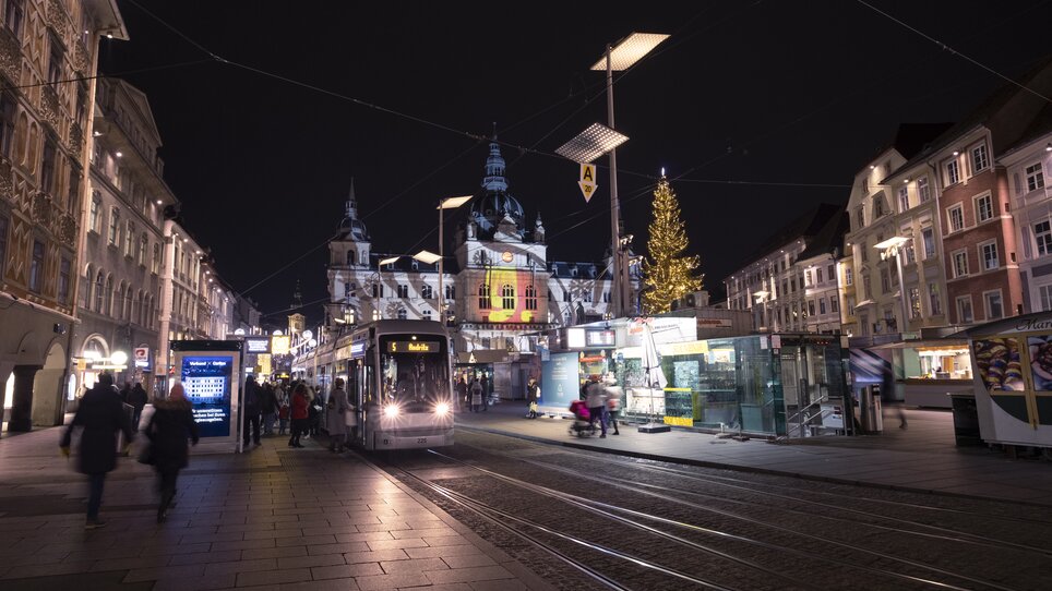 Night view of a Christmas market in Graz with tram and festively illuminated buildings. | © Vincent Croce