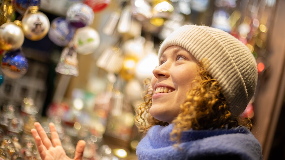 A smiling woman looks at Christmas decorations at a market. | © Graz Tourismus - Harry Schiffer