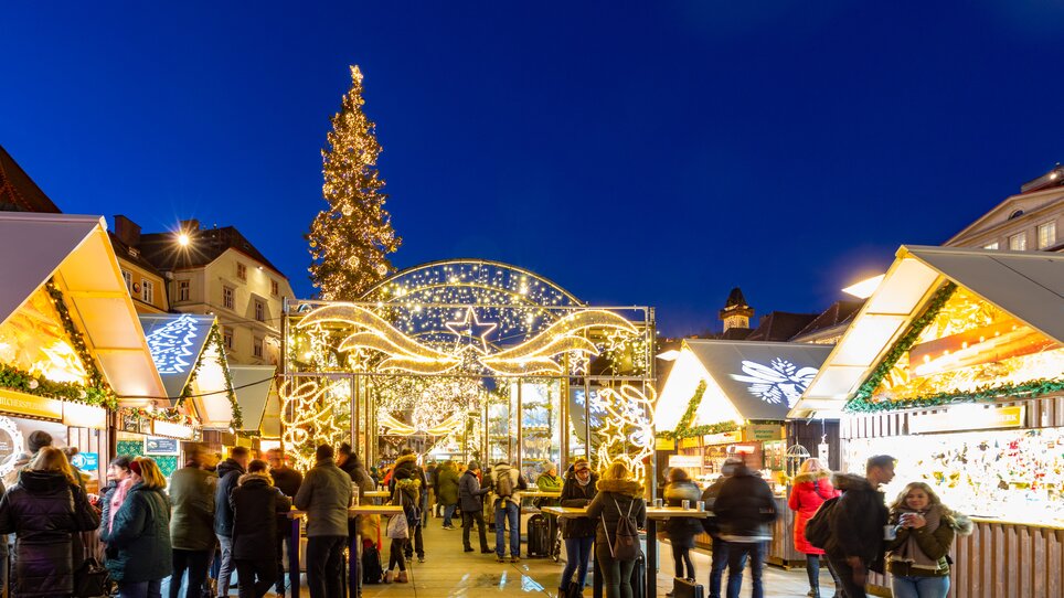 Christmas market in Graz with festive lighting, decorated stalls, and a large Christmas tree. | © Graz Tourismus - Harry Schiffer