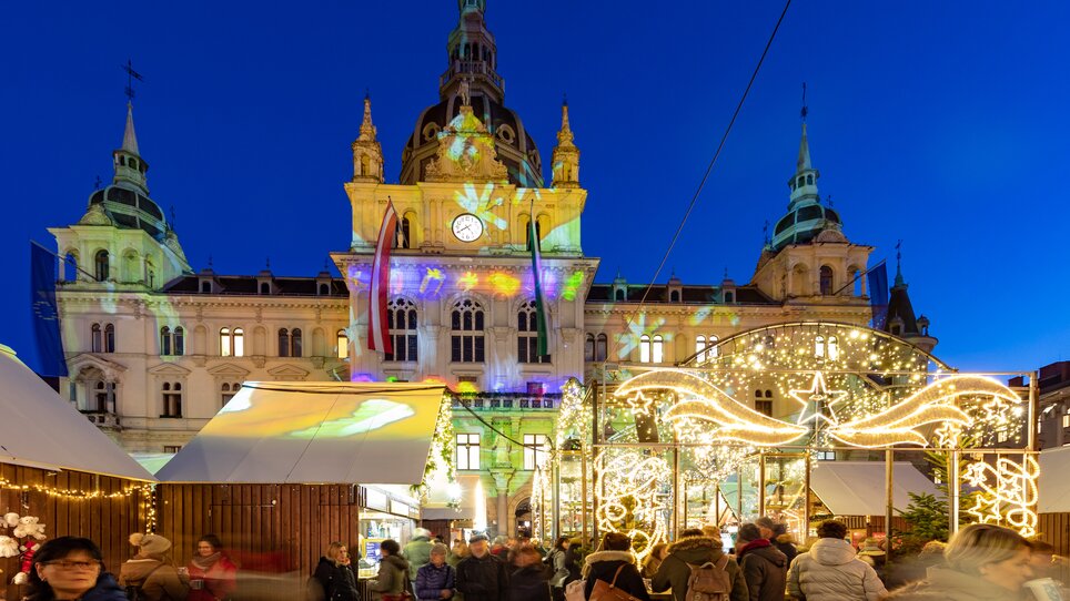 Illuminated Christmas market bustling with people in front of Graz City Hall during the festive season. | © Graz Tourismus - Harry Schiffer