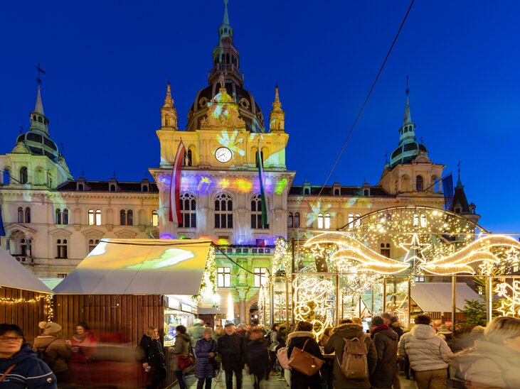 Beleuchteter Christkindlmarkt mit Menschen vor dem Grazer Rathaus zur Weihnachtszeit. | © Graz Tourismus - Harry Schiffer