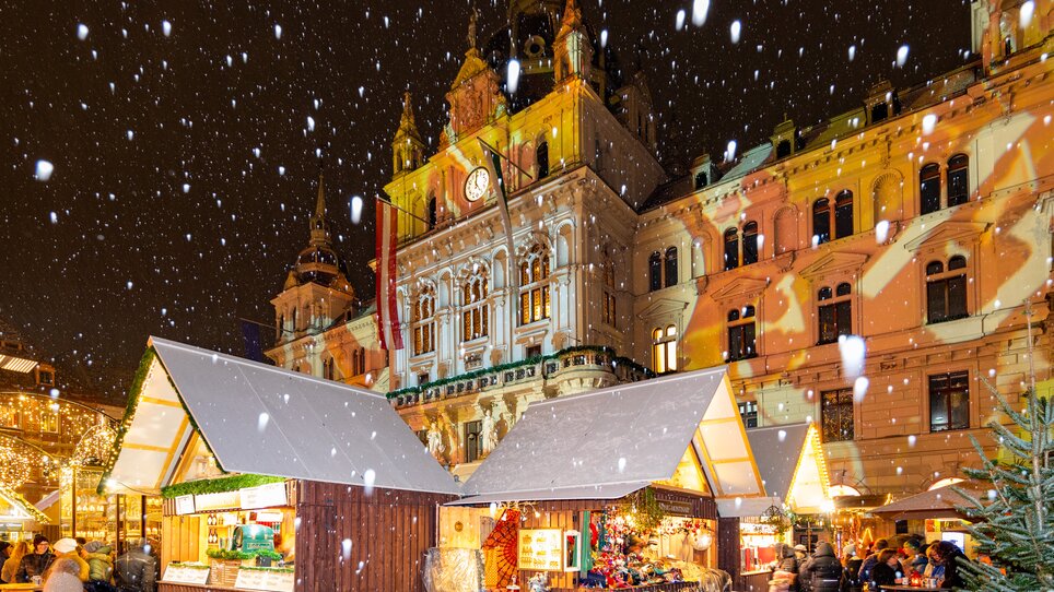 Christmas market in Graz with festively lit stalls and snow-covered town hall. | © Graz Tourismus-Harry Schiffer