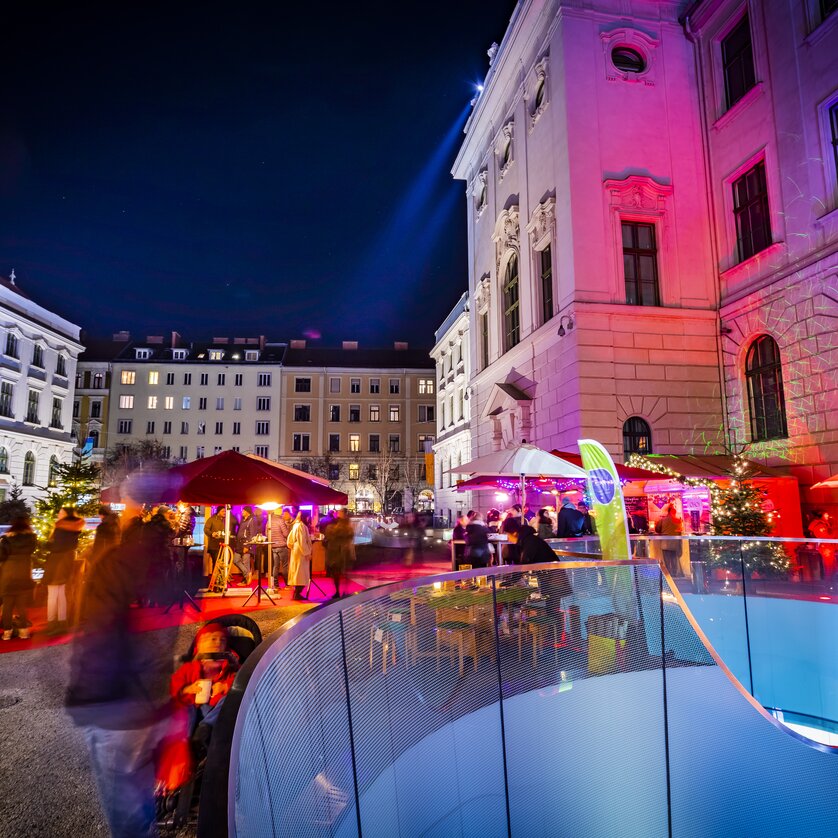 Verschiedene Stände und festliche Beleuchtung im Joanneumsviertel von Graz, umgeben von historischen Gebäuden und einer lebendigen Atmosphäre. | © Graz Tourismus - Werner Krug
