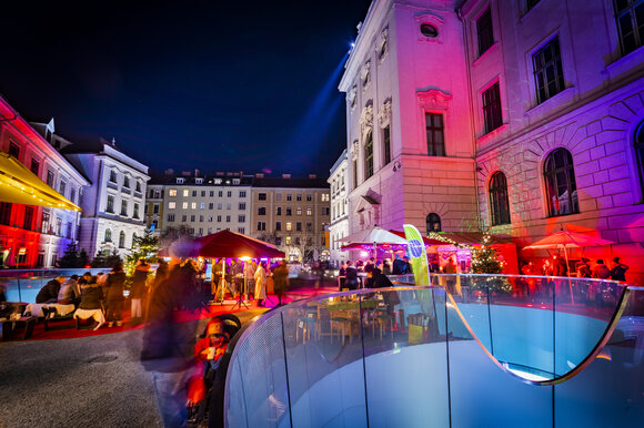 Vari stand e luci festive nel quartiere Joanneum di Graz, circondati da edifici storici e un'atmosfera vivace. | © Graz Tourismus - Werner Krug