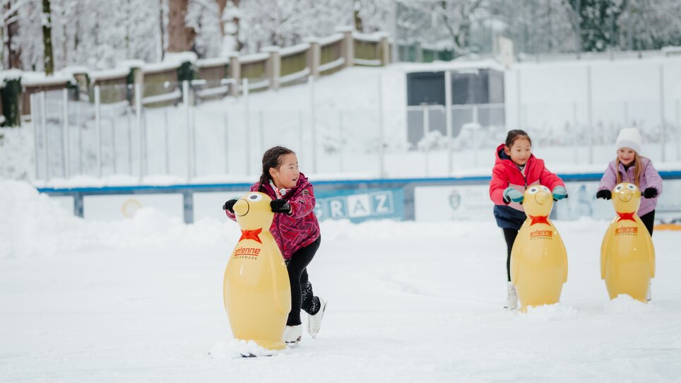 Children skating on the ice rink, using penguin aids to glide. | © Daniel Kindler