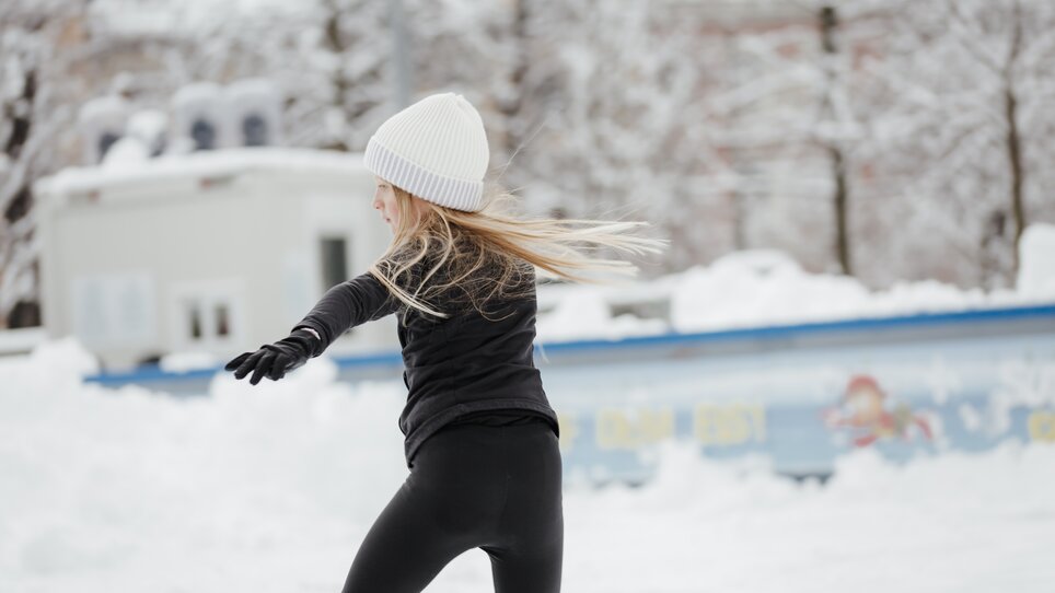 A girl with long blonde hair and a white beanie skating on an ice rink in winter. | © Daniel Kindler