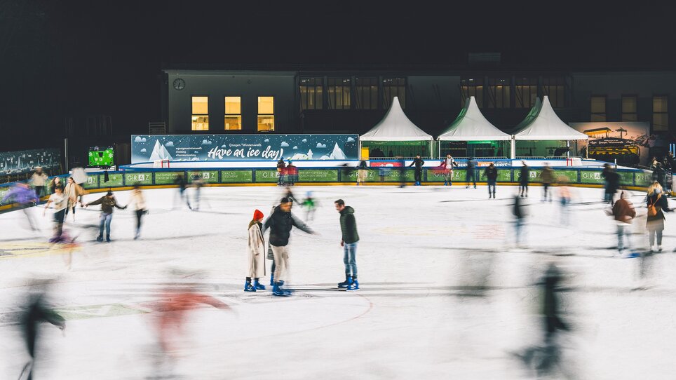People skating on a brightly lit ice rink at night. | © Luke Goodlife