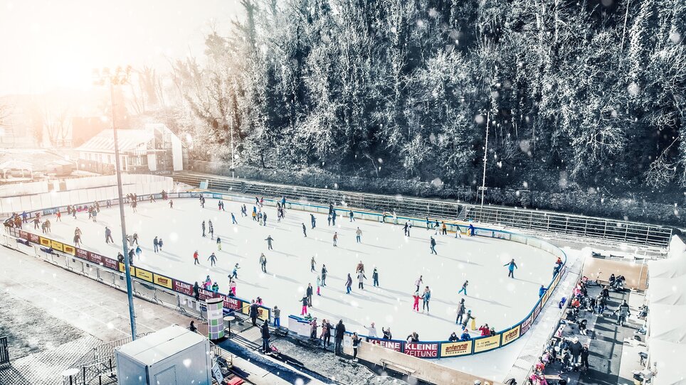People skate on a lit ice rink in Graz, surrounded by a winter landscape. | © Simon Möstl