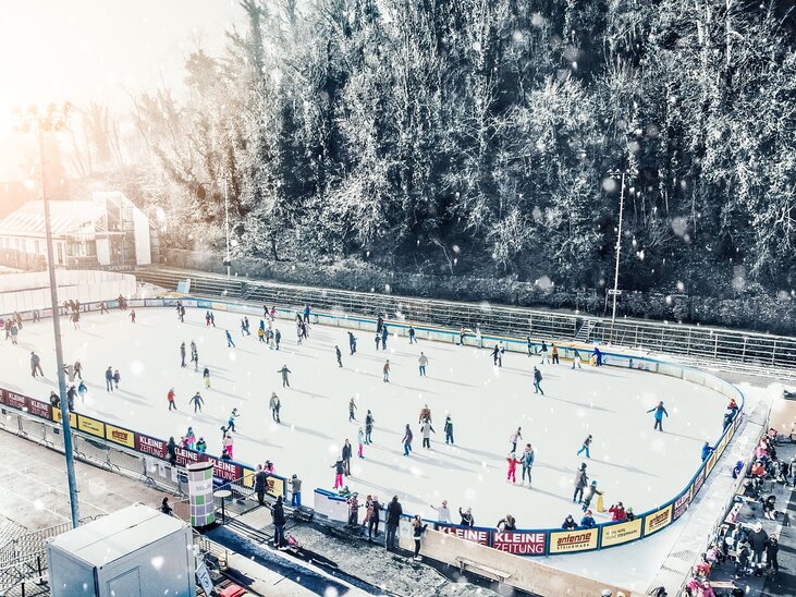 Menschen beim Eislaufen auf einem beleuchteten Eislaufplatz in Graz, umgeben von winterlicher Landschaft. | © Simon Möstl