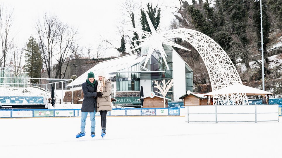 A couple ice skating on the rink in Graz, with Christmas decorations in the background. | © Graz Tourismus - Mias Photoart
